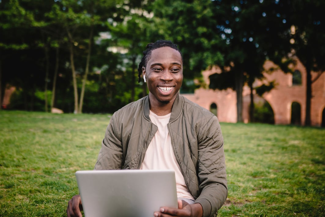 Cheerful man with laptop and wireless earphones in park